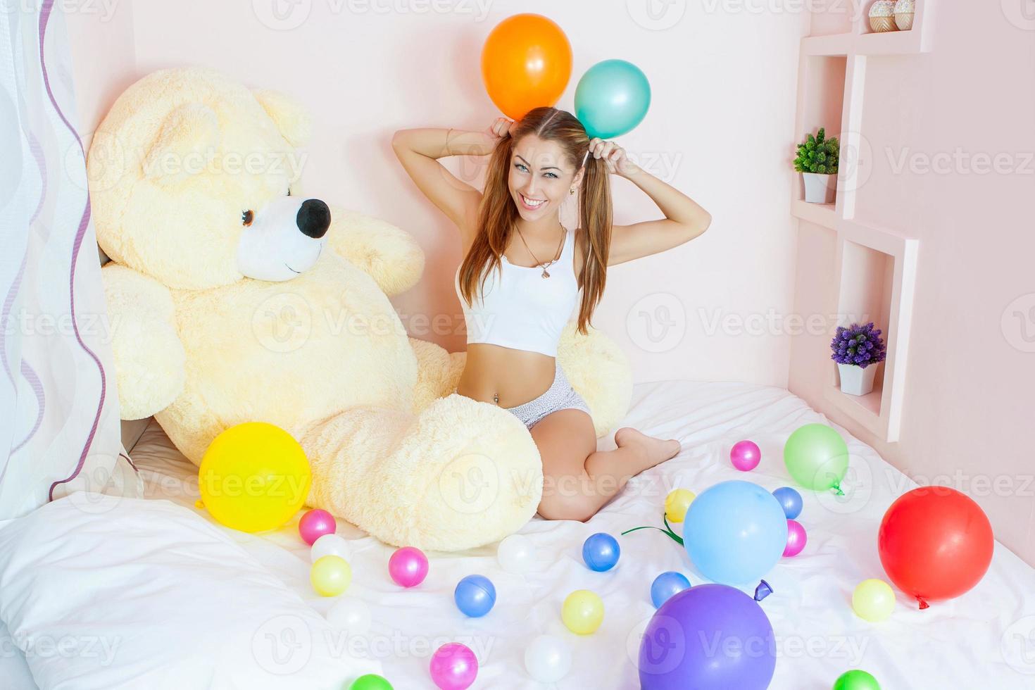 vrouw aan bed met grote speelgoedbeer en kleurrijke ballen. foto
