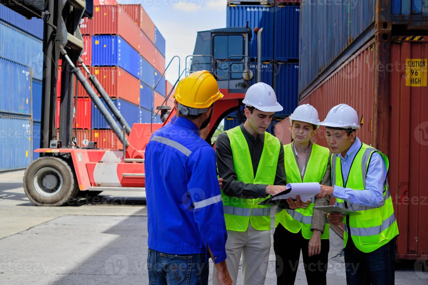 een groep multiraciale arbeidersmensen in veiligheidsuniformen en veiligheidshelmen werken op een logistieke terminal met veel stapels containers, en laden controleverzendingsgoederen voor de vrachtvervoersindustrie. foto