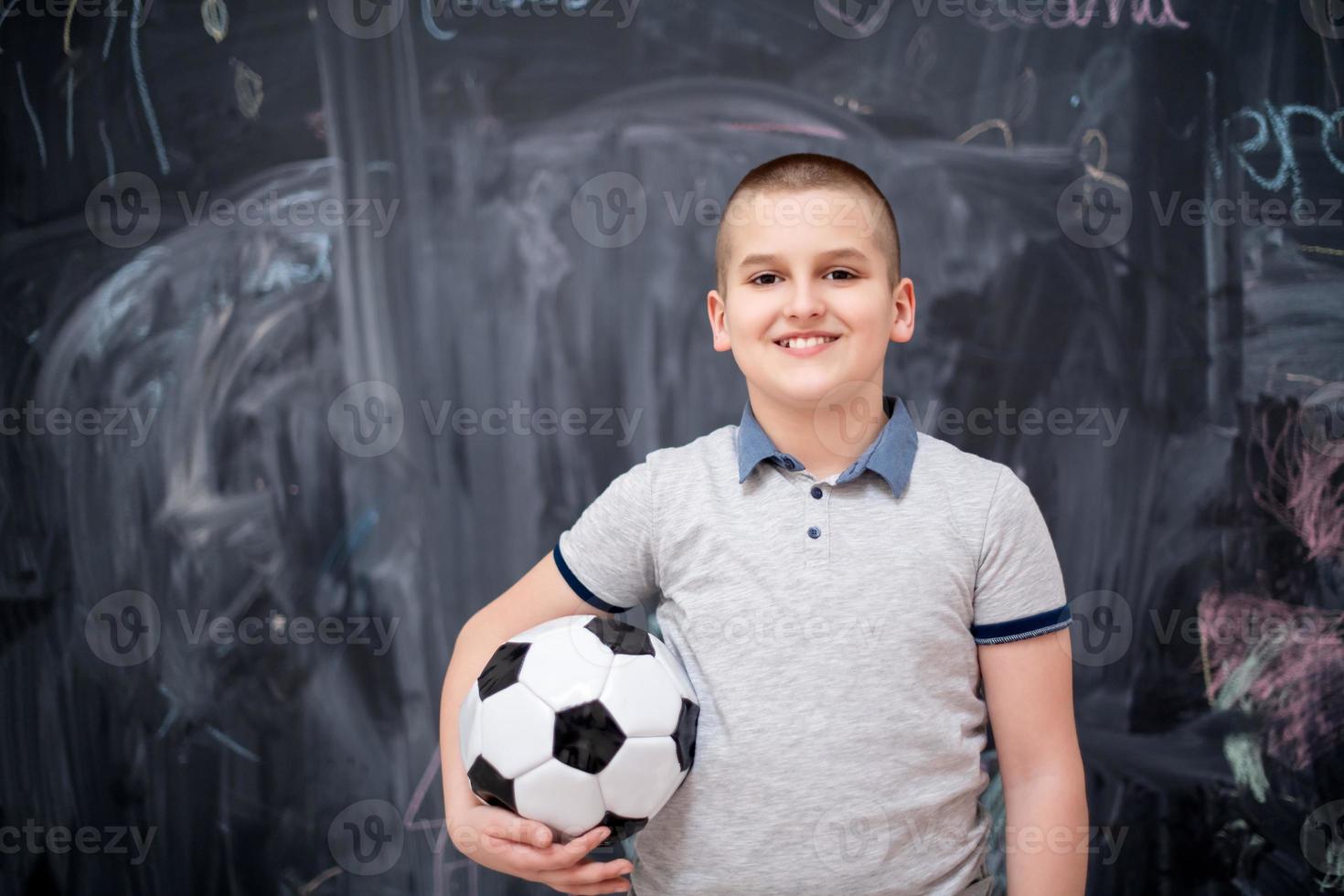 gelukkige jongen die een voetbal voor schoolbord houdt foto