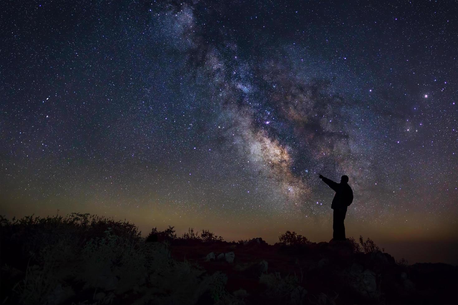 een man staat naast het melkwegstelsel wijzend op een heldere ster, foto met lange sluitertijd, met korrel
