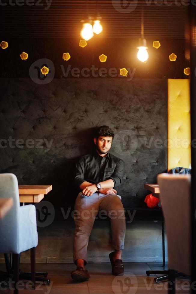 zelfverzekerde jonge Indiase man in zwart shirt zit in café. foto