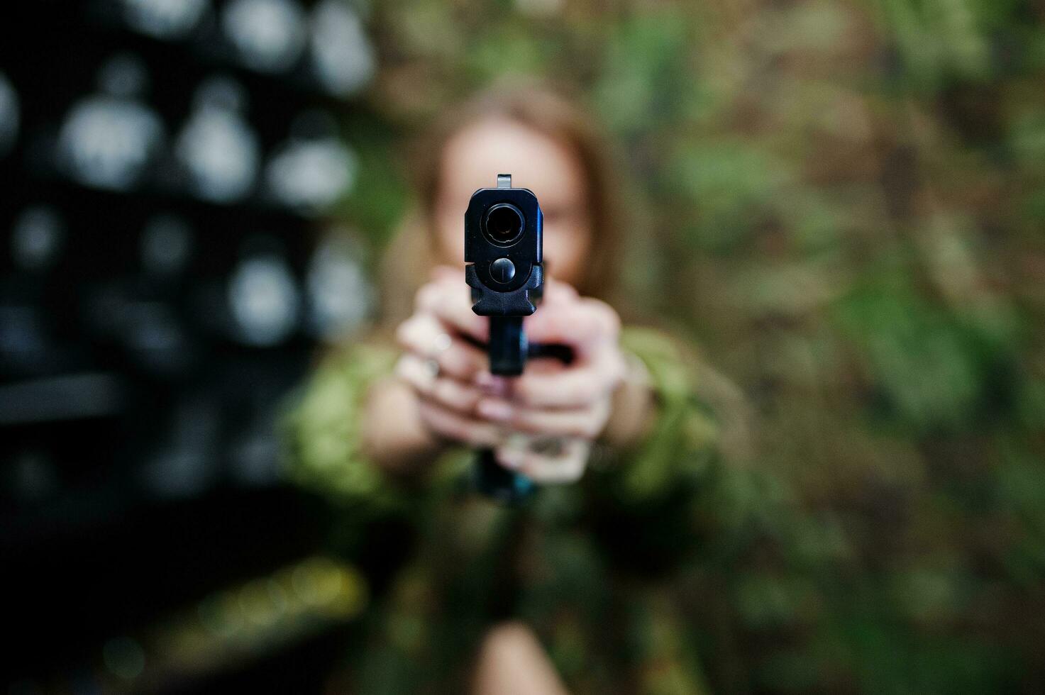 militair meisje in camouflage uniform met pistool bij de hand tegen leger achtergrond op schietbaan. focus op pistool. foto