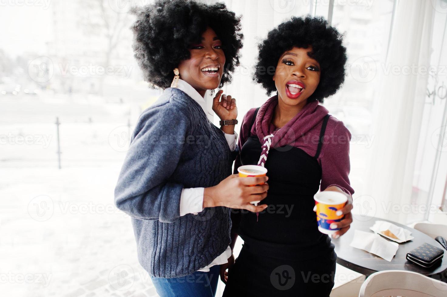 twee Afro-Amerikaanse vrouw met krullend haar draagt truien met kopjes thee in café binnen. foto