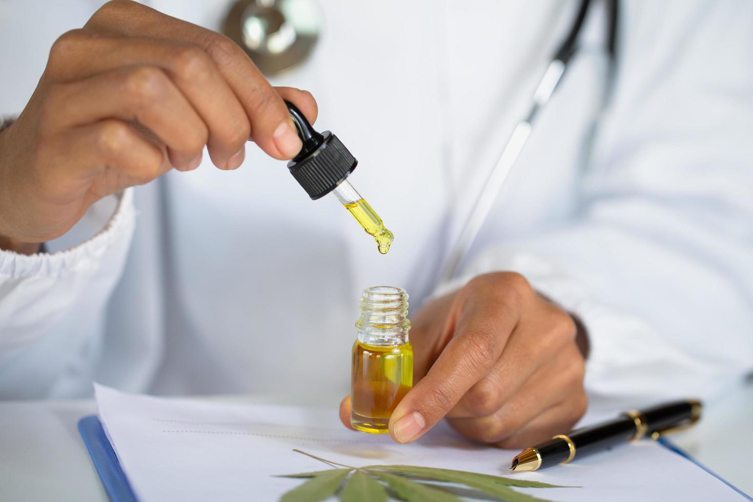dokter handen met een druppelaar met een olieproduct op de achtergrond van de bladeren en marihuanabloemen, cbd hennepolie. foto