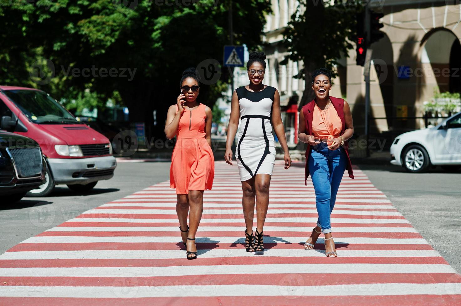 drie stijlvolle afro-amerikaanse dames lopen op zebrapad of zebrapad, spreken elkaar en hebben plezier. foto