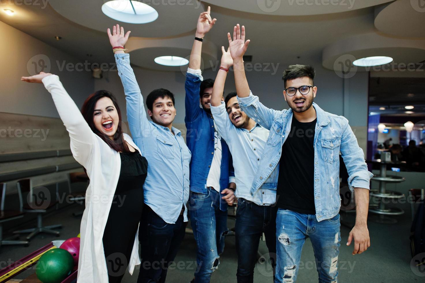 groep van vijf Zuid-Aziatische volkeren die rust en plezier hebben bij de bowlingclub. handen omhoog, juichen en juichen. foto