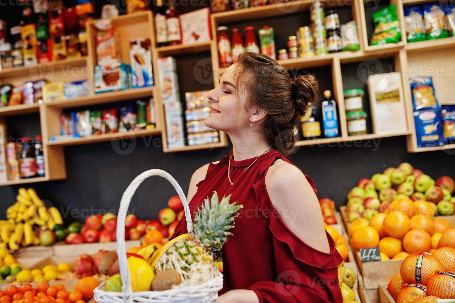 meisje in het rood met verschillende groenten en fruit in de mand in de fruitwinkel. foto