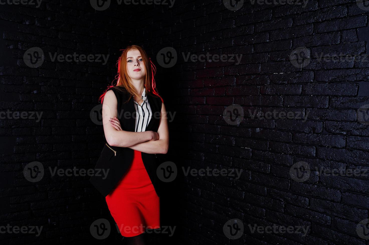 portret van een aantrekkelijk roodharig meisje in slevelless jasje, gestreepte blouse en rode broek poseren naast de bakstenen muur. foto