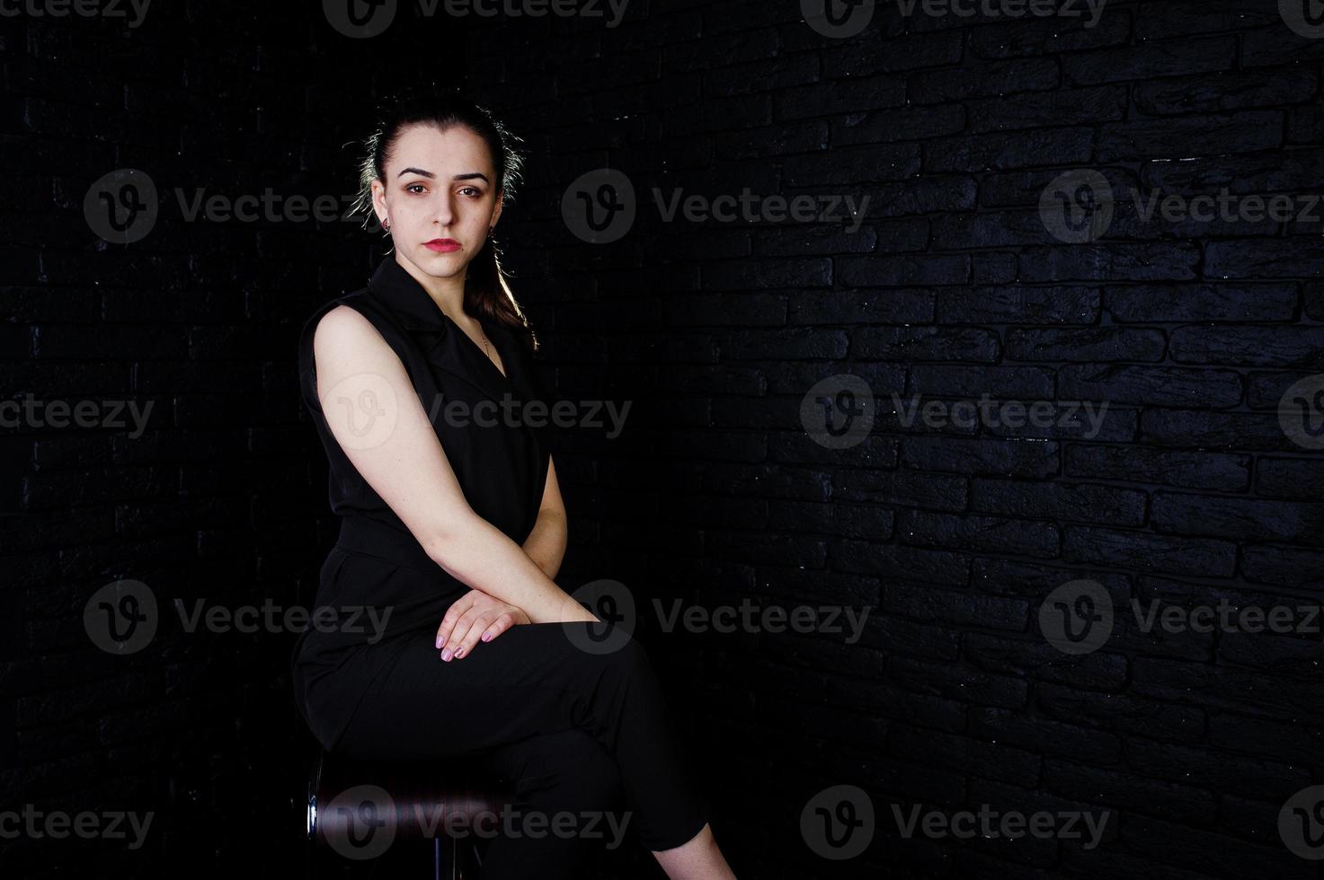 portret van een mooie brunette meisje in zwarte jumpsuit zitten en poseren in de studio. foto