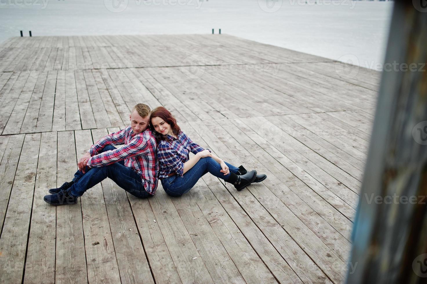 stijlvolle paar slijtage op geruit hemd verliefd samen zittend op de pier. foto