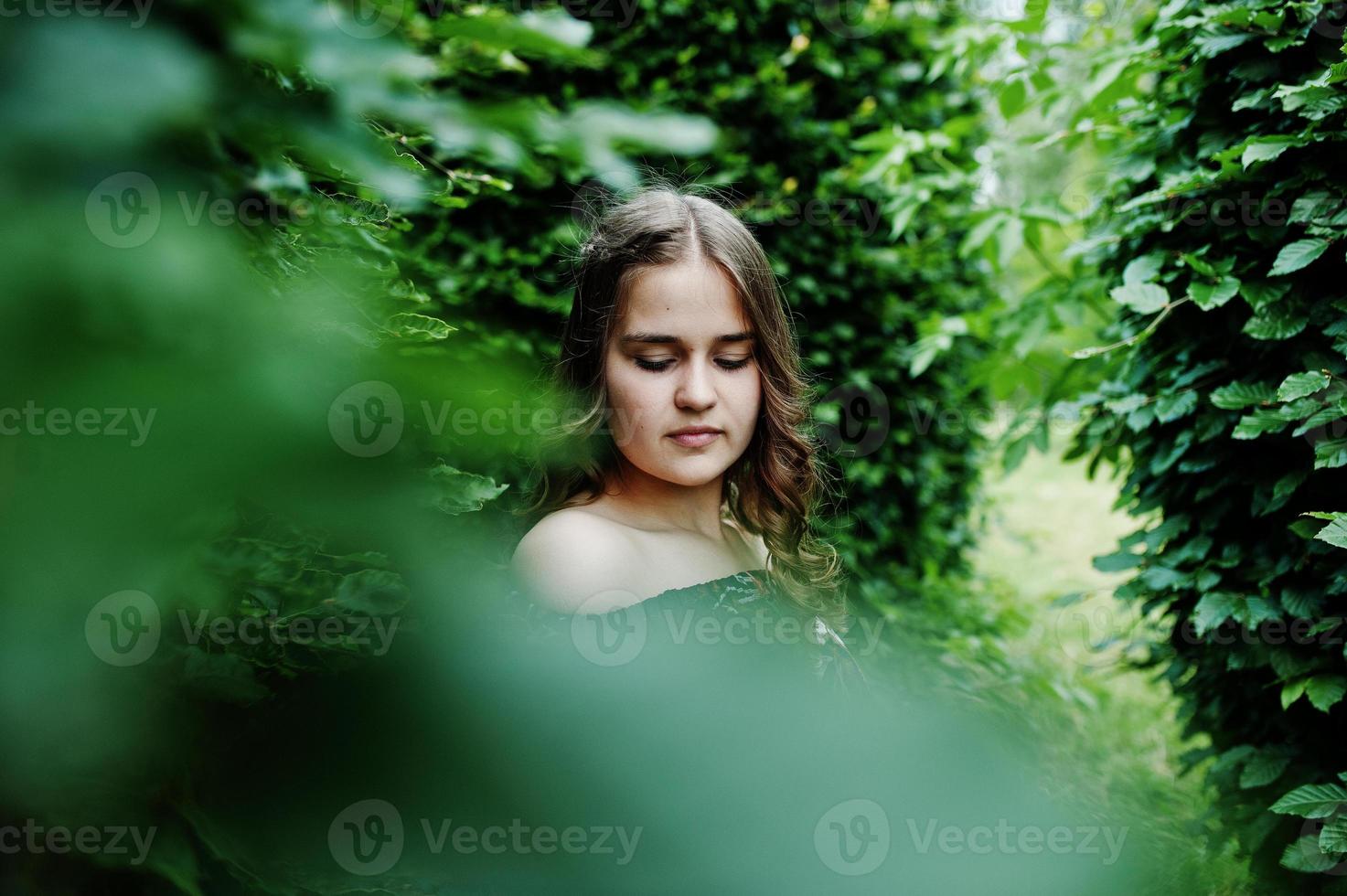 portret van een fantastisch jong meisje in mooie jurk met stijlvol krullend kapsel poseren in het bos of park. foto