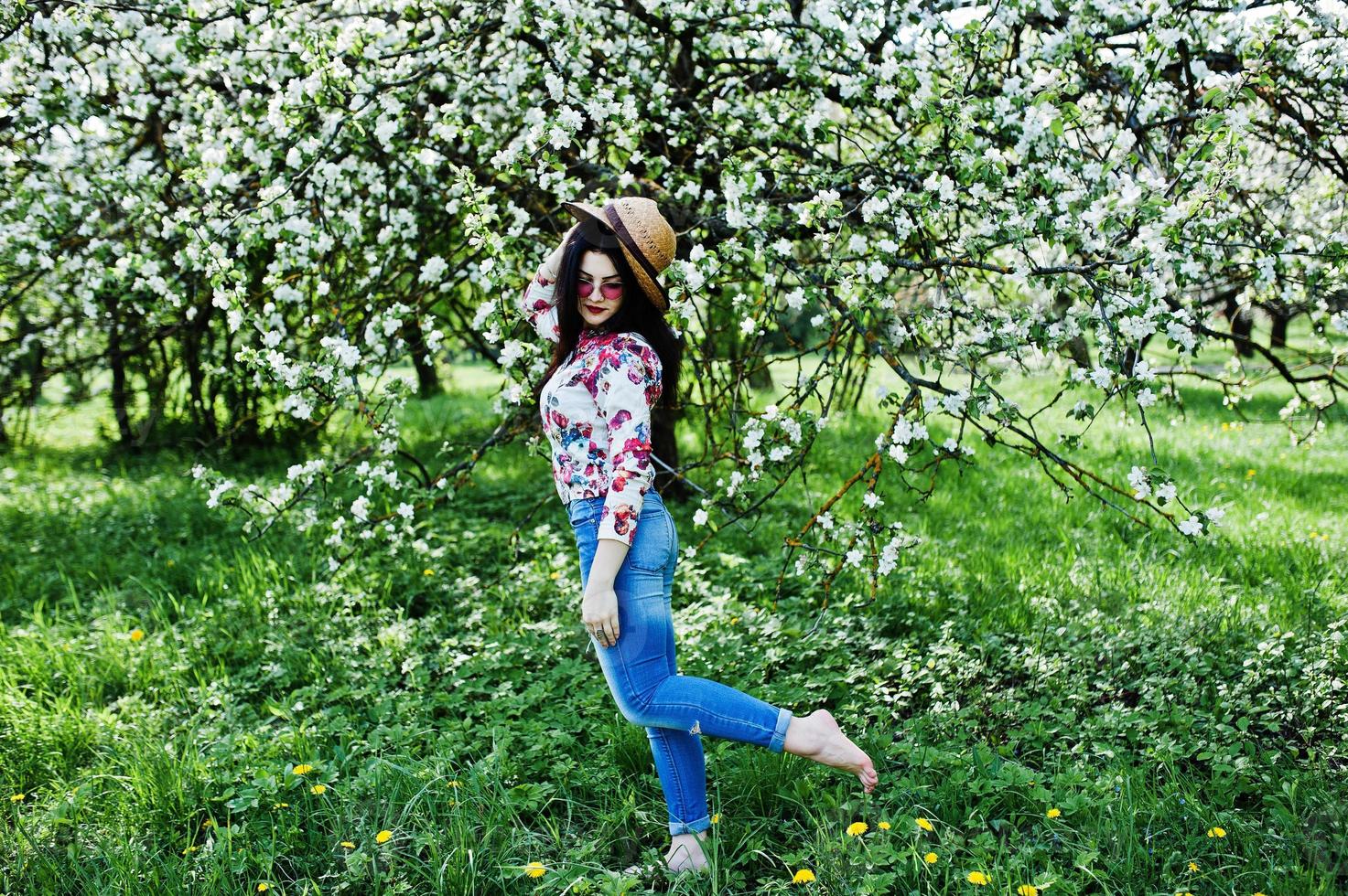 lente portret van brunette meisje in roze bril en hoed op groene bloesem tuin. foto