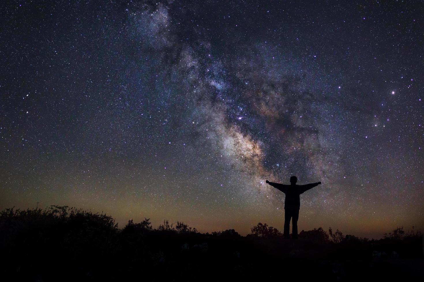 landschap met melkweg, nachtelijke hemel met sterren en silhouet van een staande gelukkige man op de berg, foto met lange sluitertijd, met graan