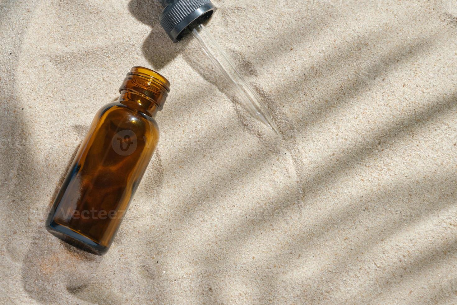 gezichtsserum van glazen fles met een pipet op een natuurlijke achtergrond met zand. etherische olie voor het hydrateren van de lichaamshuid. mockup van beauty fashion cosmetische fles dropper product met huidverzorging concept. foto