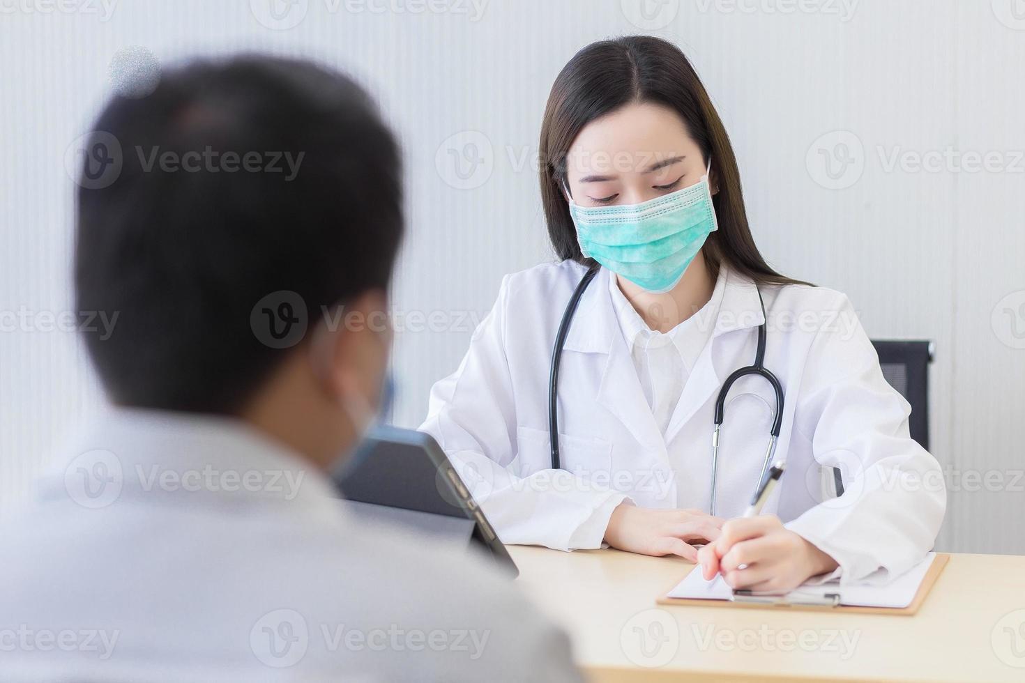 aziatische vrouw arts draagt een medisch gezichtsmasker en registreert symptoom van een man patiënt op papier in het ziekenhuis. coronavirus beschermingsconcept. foto