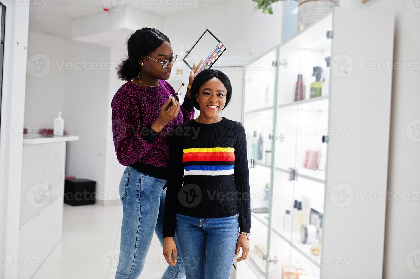 Afro-Amerikaanse vrouw die make-up toepast door visagist bij beauty salon. foto