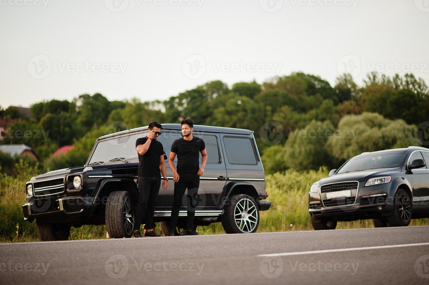 twee aziatische broers die een man dragen op alle zwarte poses in de buurt van suv-auto's. foto