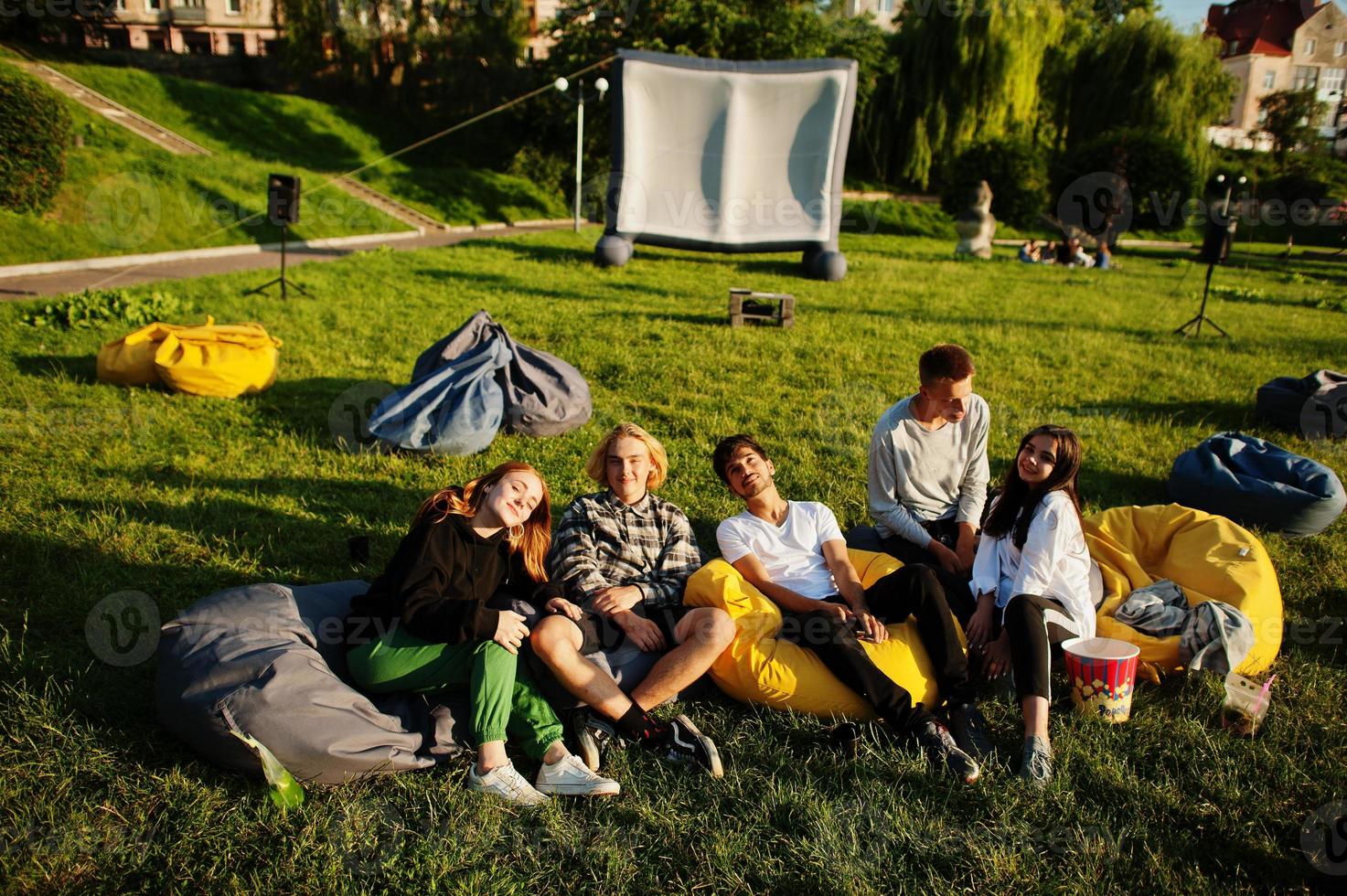 jonge multi-etnische groep mensen kijken naar film op poef in openluchtbioscoop. foto