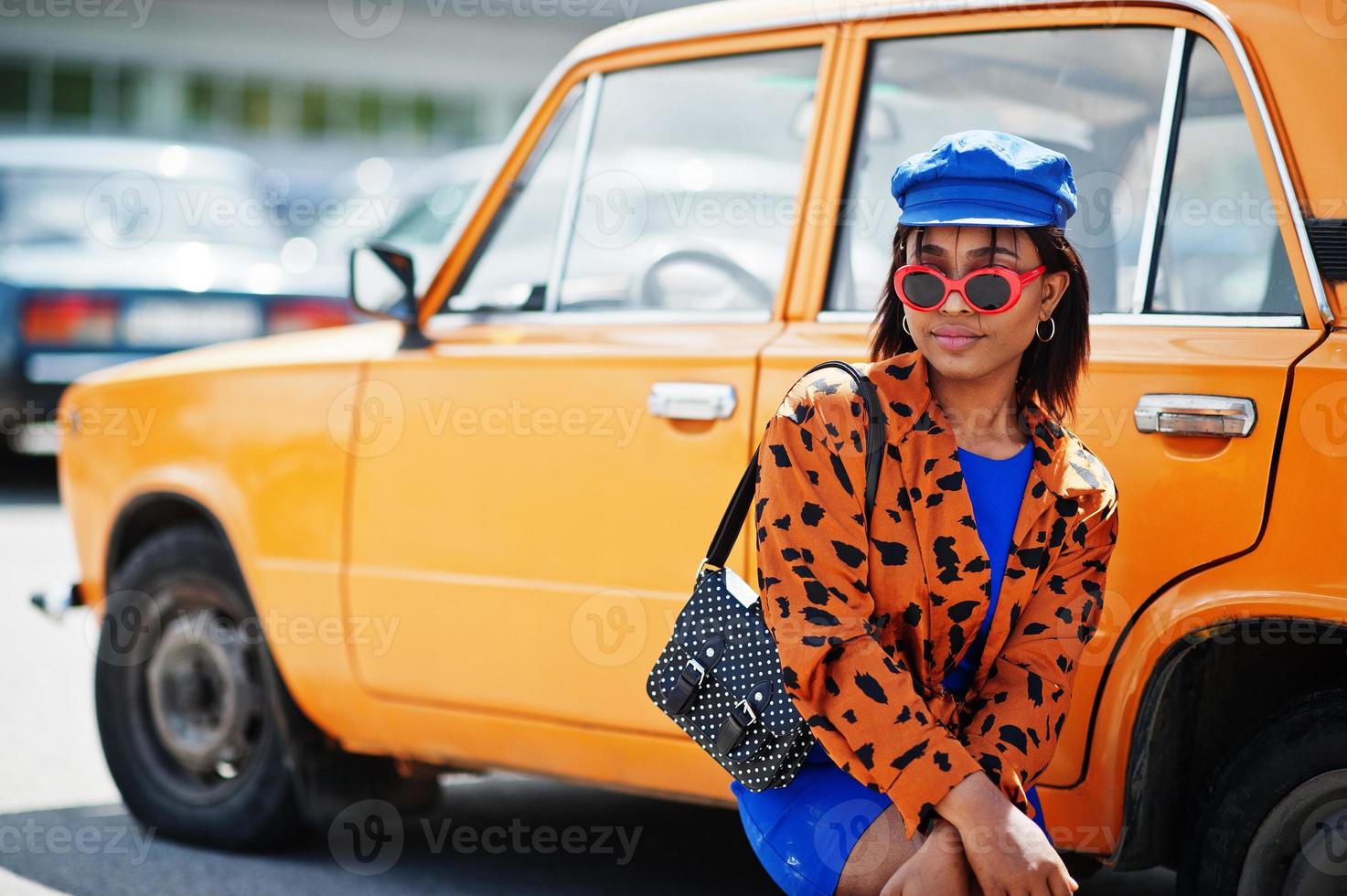 mooie afrikaanse amerikaanse dame met zonnebril die zich dichtbij oranje klassieke retro auto bevindt. foto