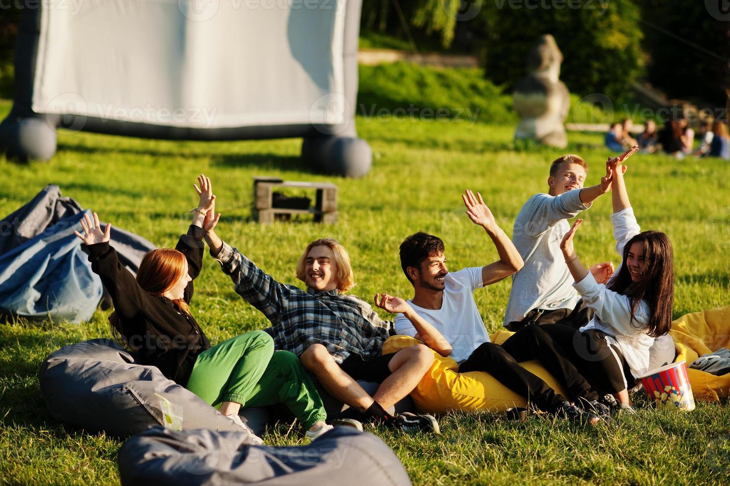 jonge multi-etnische groep mensen kijken naar film op poef in openluchtbioscoop. foto