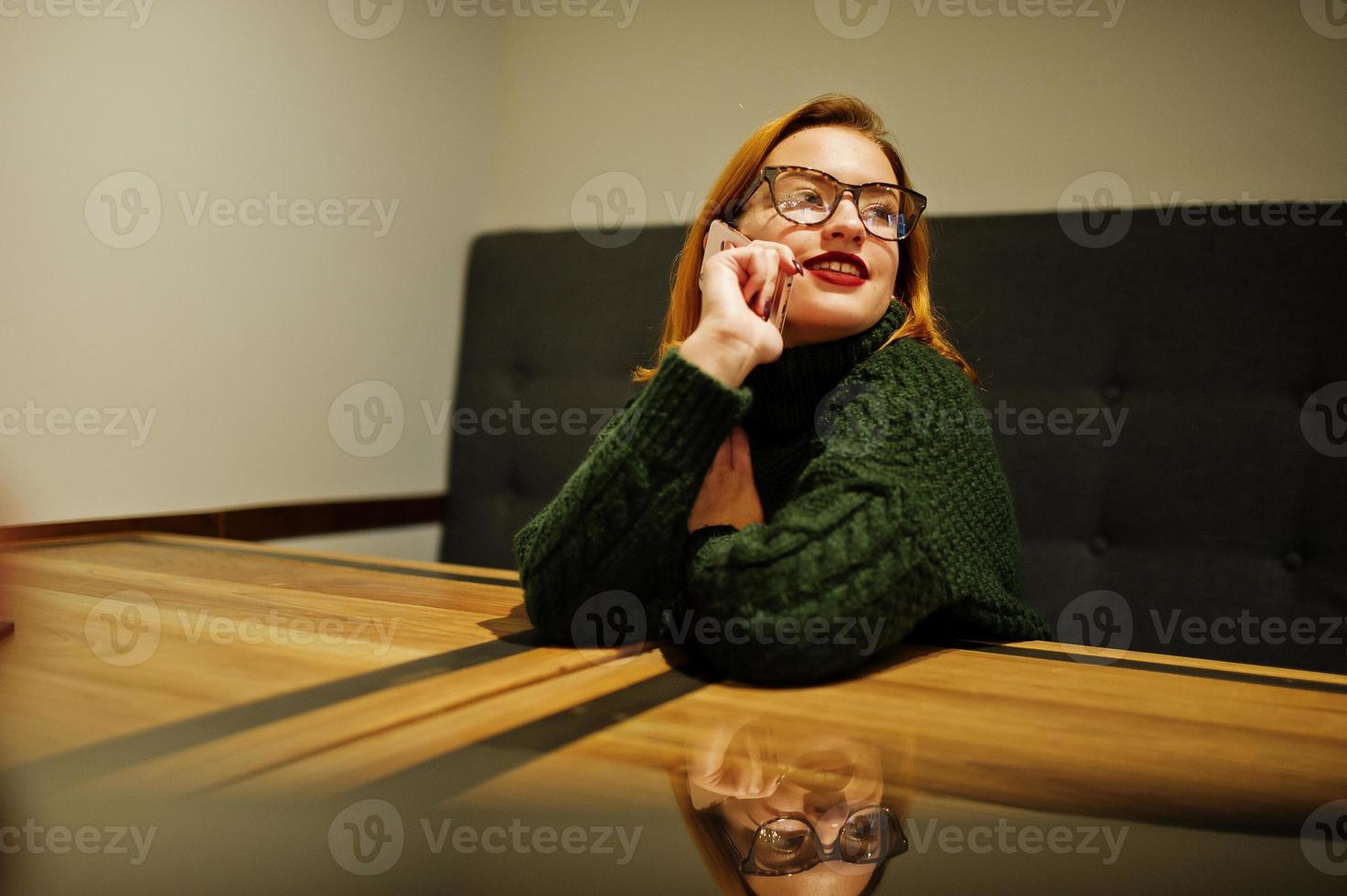 vrolijke jonge mooie roodharige vrouw in glazen, draag op groene warme wollen trui, zittend in café. foto