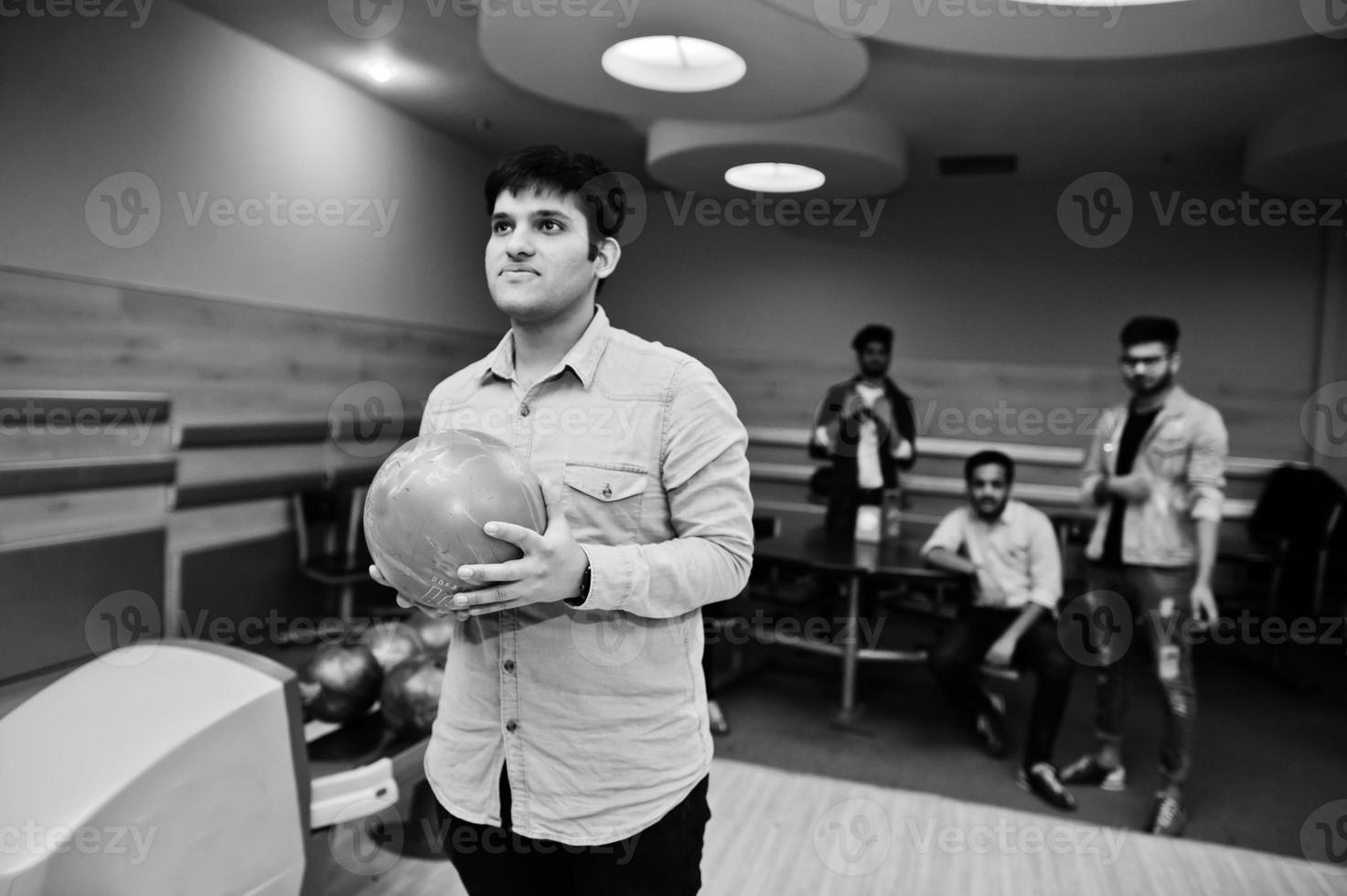 Zuid-Aziatische man in jeans shirt staande op bowlingbaan met bal op handen. man bereidt zich voor op een worp. foto