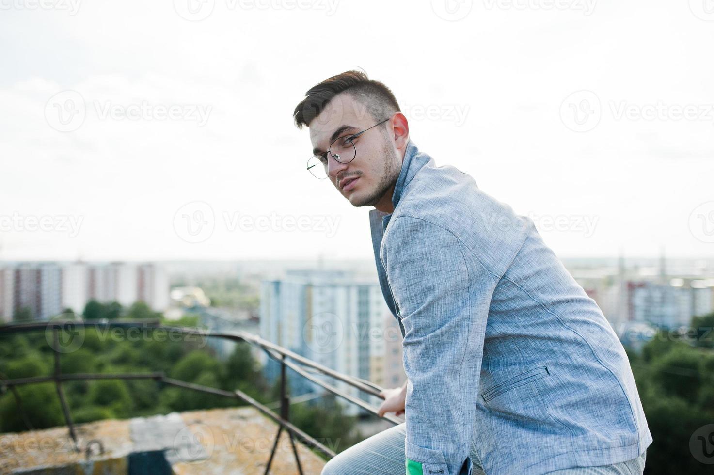 dromer stijlvolle macho man in grijs pak en bril op het dak. foto