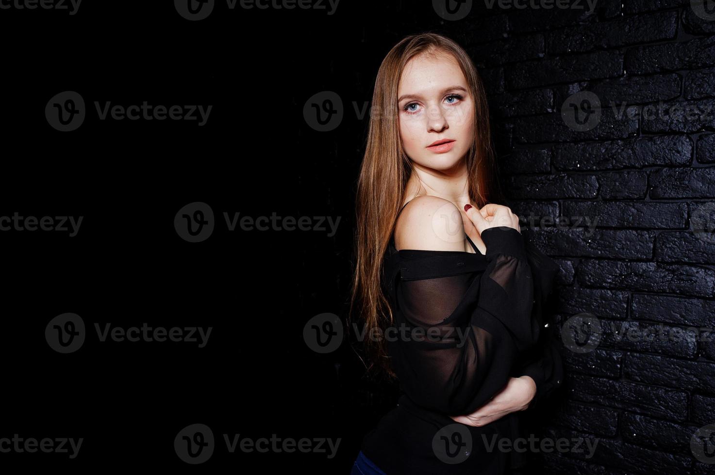 studio shot van brunette meisje in zwarte blouse met beha en korte broek tegen zwarte bakstenen muur. foto