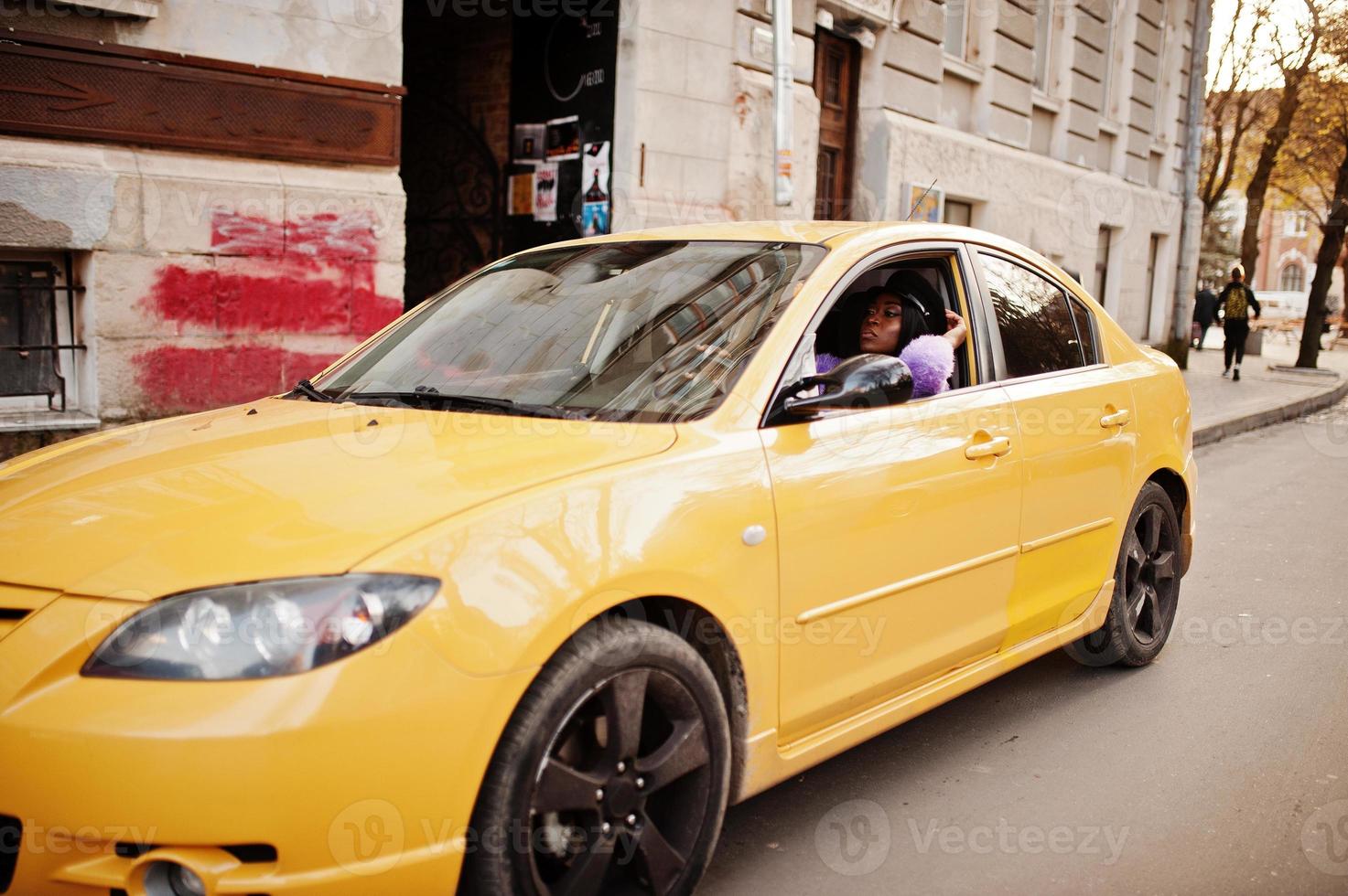 Afro-Amerikaanse vrouw op violette jurk en pet poseerde bij gele auto. foto