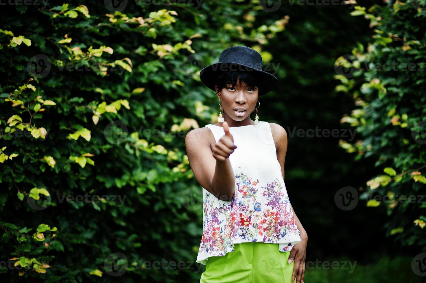 geweldige Afro-Amerikaanse modelvrouw in groene broek en zwarte hoed poseerde met verschillende emoties in het park, toont een duim omhoog. foto