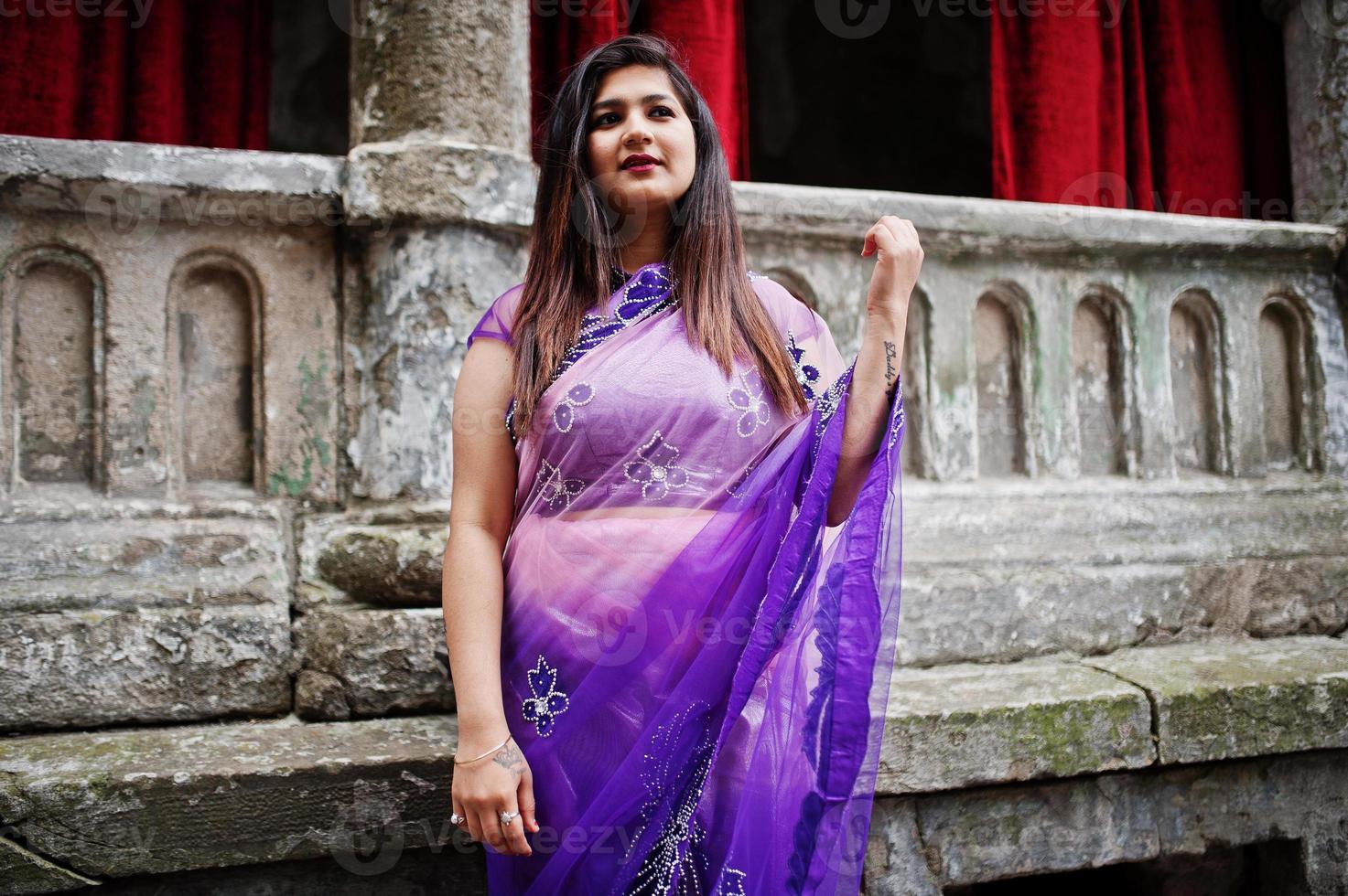 indiase hindoe meisje op traditionele violet saree poseerde op straat tegen oud huis met rode gordijnen. foto