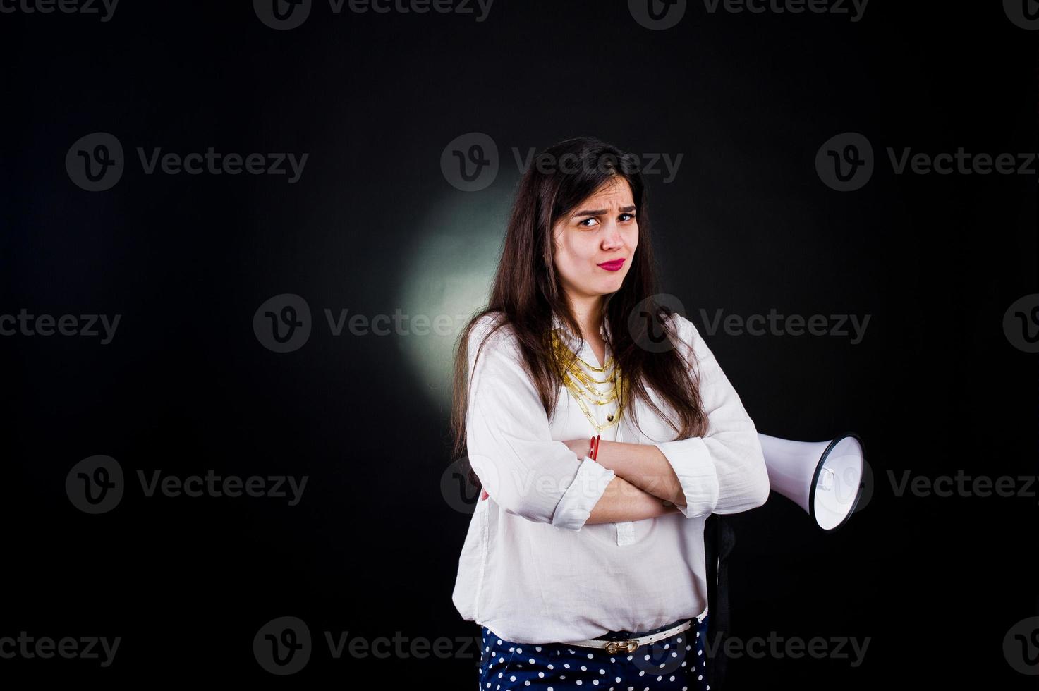 portret van een jonge vrouw in blauwe broek en witte blouse poseren met megafoon in de studio. foto