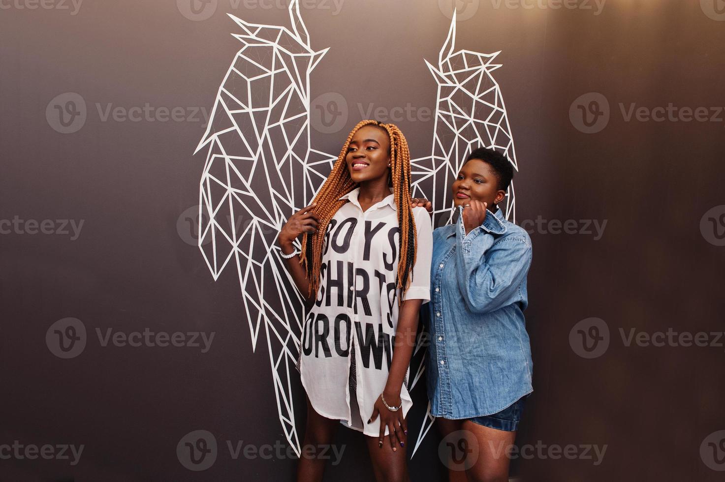 twee afrikaanse dames in stijlvolle casual kleding poseren tegen de muur van engelenvleugels. foto