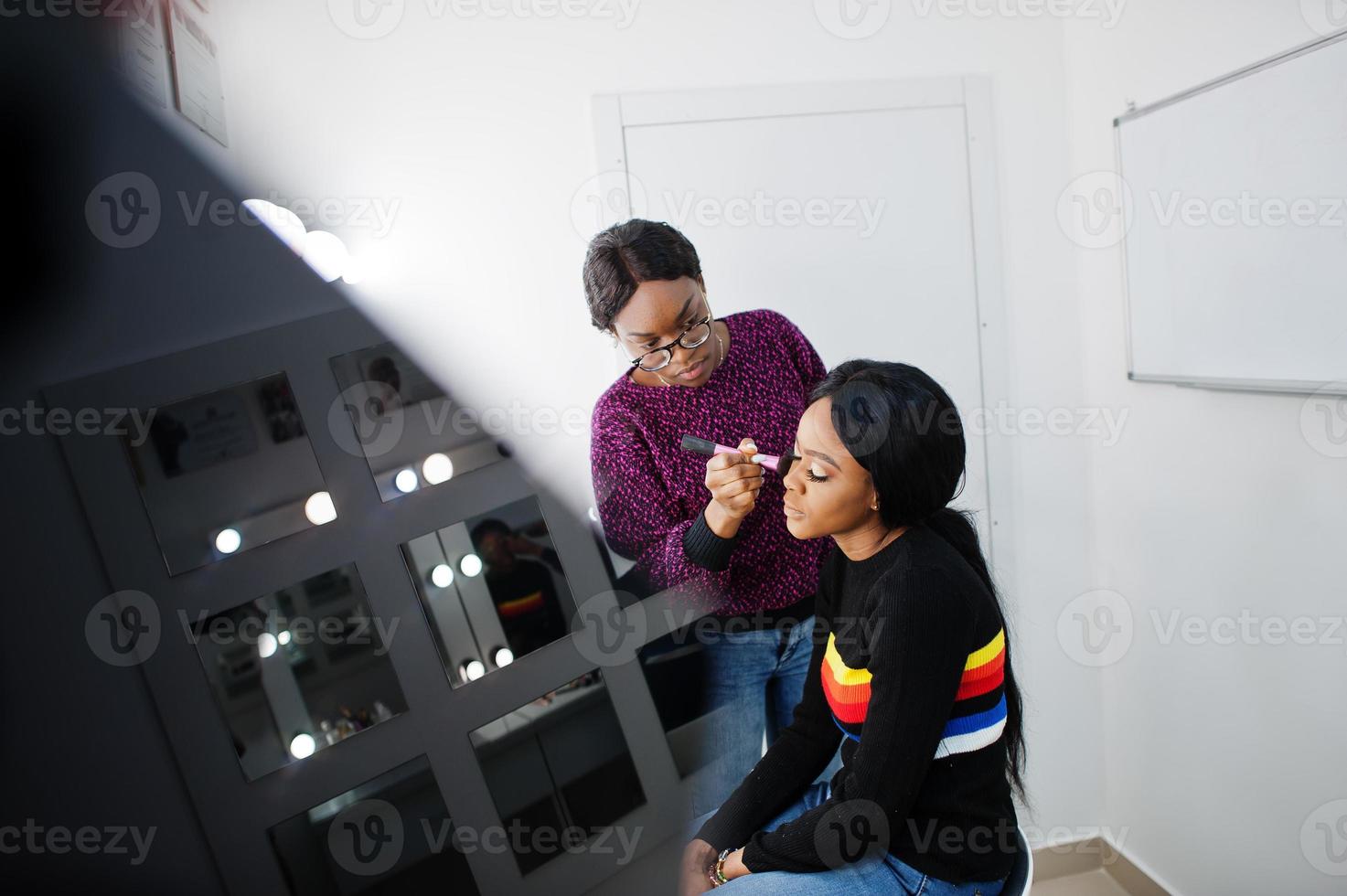 Afro-Amerikaanse vrouw die make-up toepast door visagist bij beauty salon. foto