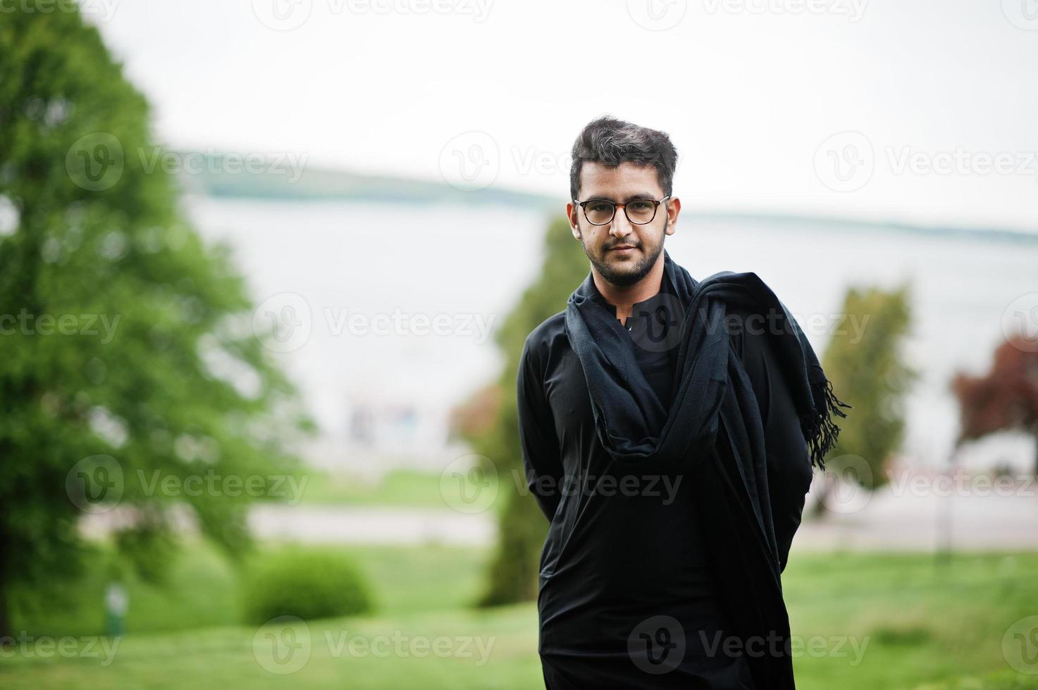 pakistaans bangladesh man draagt zwarte traditionele kleding en een bril poseert buiten. foto