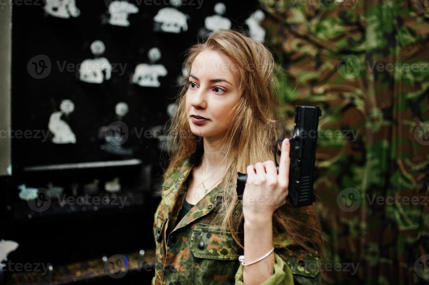 militair meisje in camouflage uniform met pistool bij de hand tegen leger achtergrond op schietbaan. foto