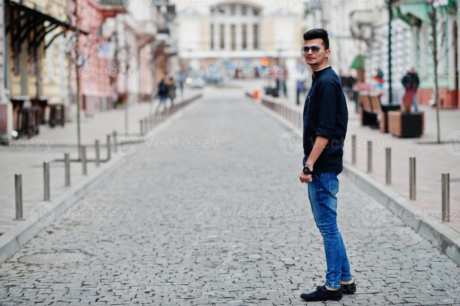 stijlvolle Indiase model man in casual kleding, zwart shirt en zonnebril poseerde buiten op straat van india. foto