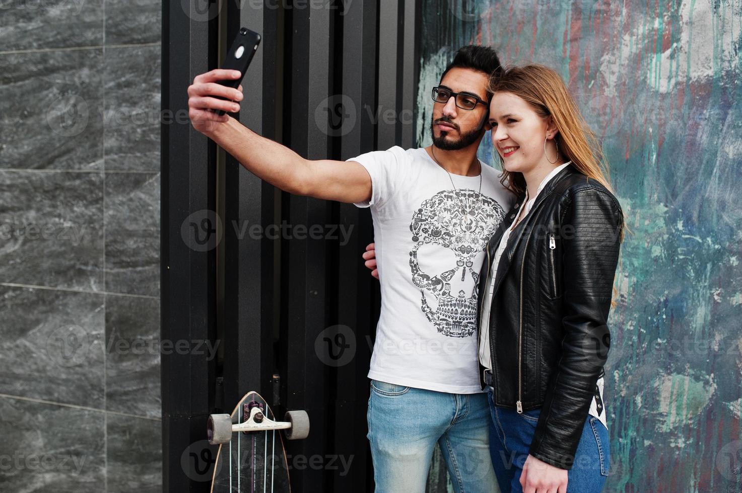 cool multiraciaal paar poseren tegen de muur en samen selfie maken. foto