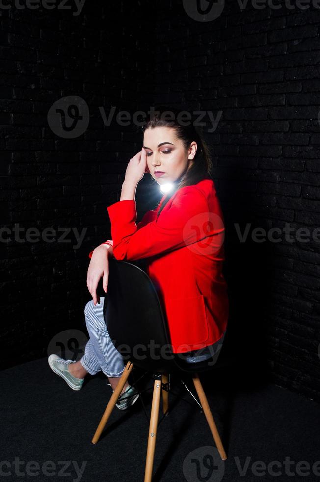 stijlvolle brunette meisje op rode jas tegen studio zwarte bakstenen muur. foto
