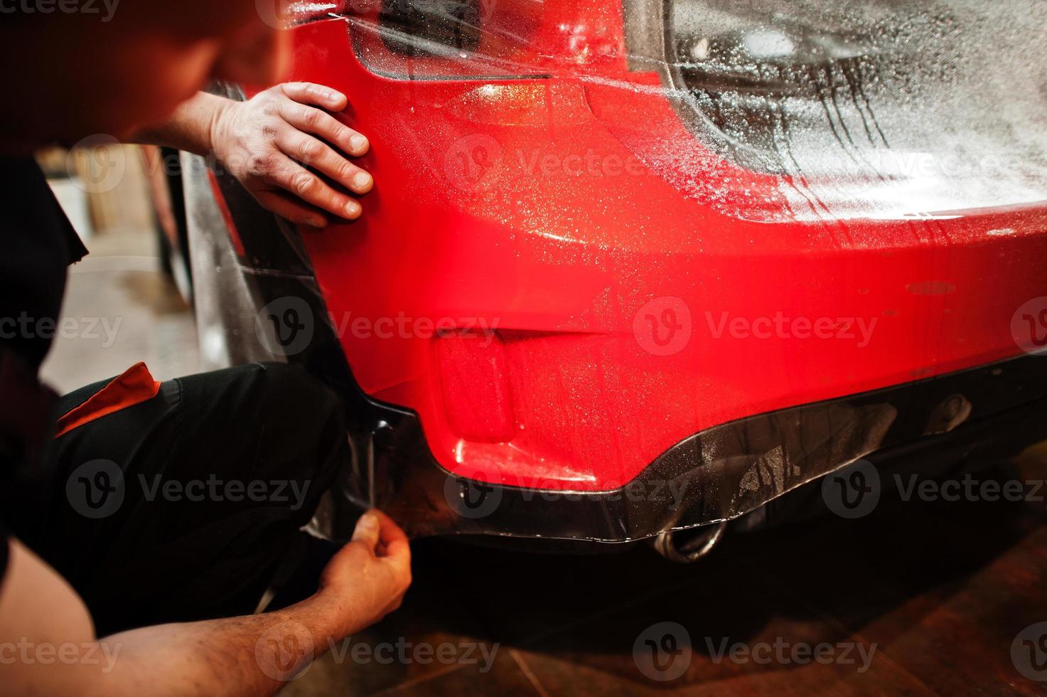 autoservicemedewerker plaatste anti-grindfilm op een rode carrosserie in de detailleringsvoertuigwerkplaats. autobescherming met speciale folies. foto