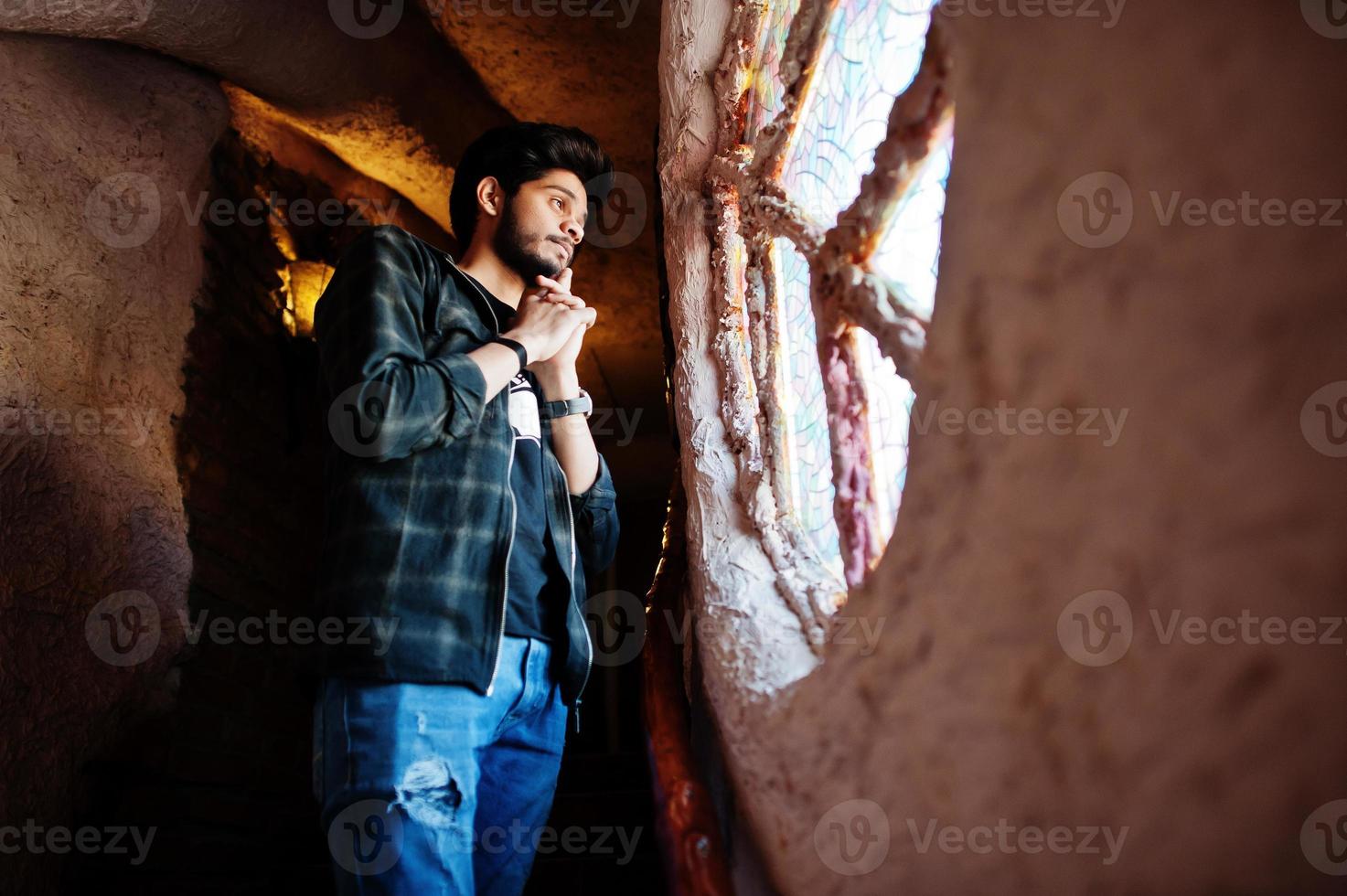 baard aziatische man in vrijetijdskleding staat in huis op trappen tegen raam. foto