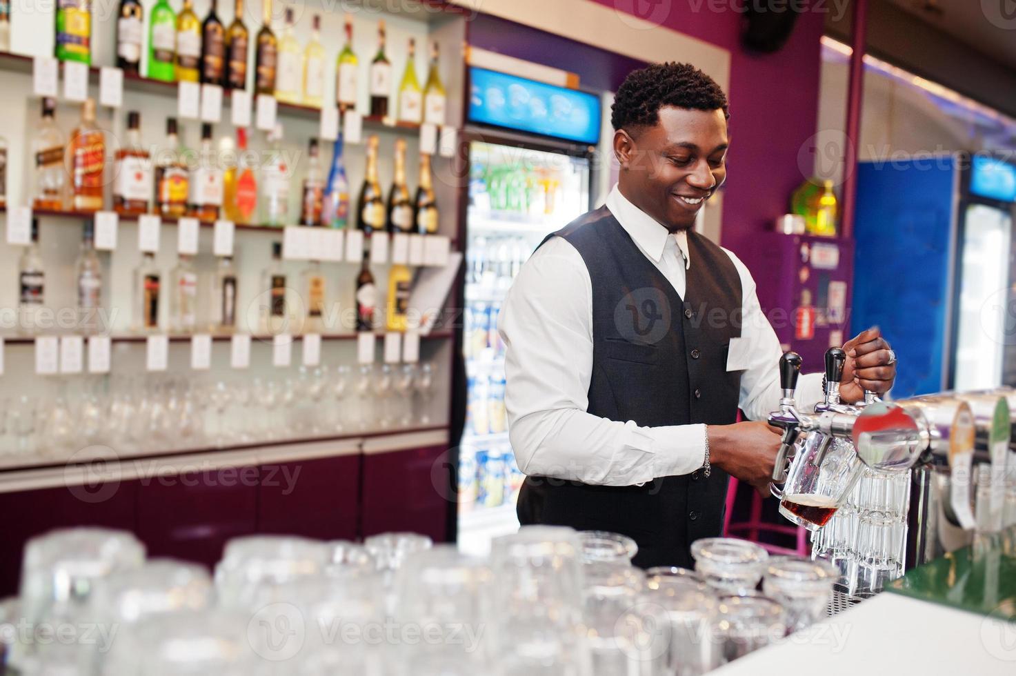 Afro-Amerikaanse barman aan de bar die van vers tapbier in het glas in de pub giet. foto