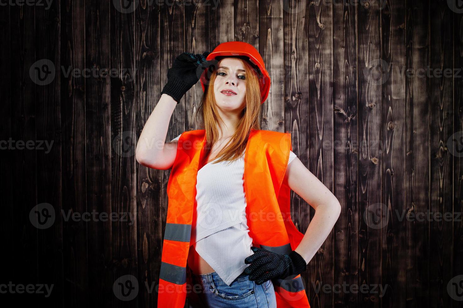 ingenieursvrouw in oranje beschermt helm en bouwjas tegen houten achtergrond. foto