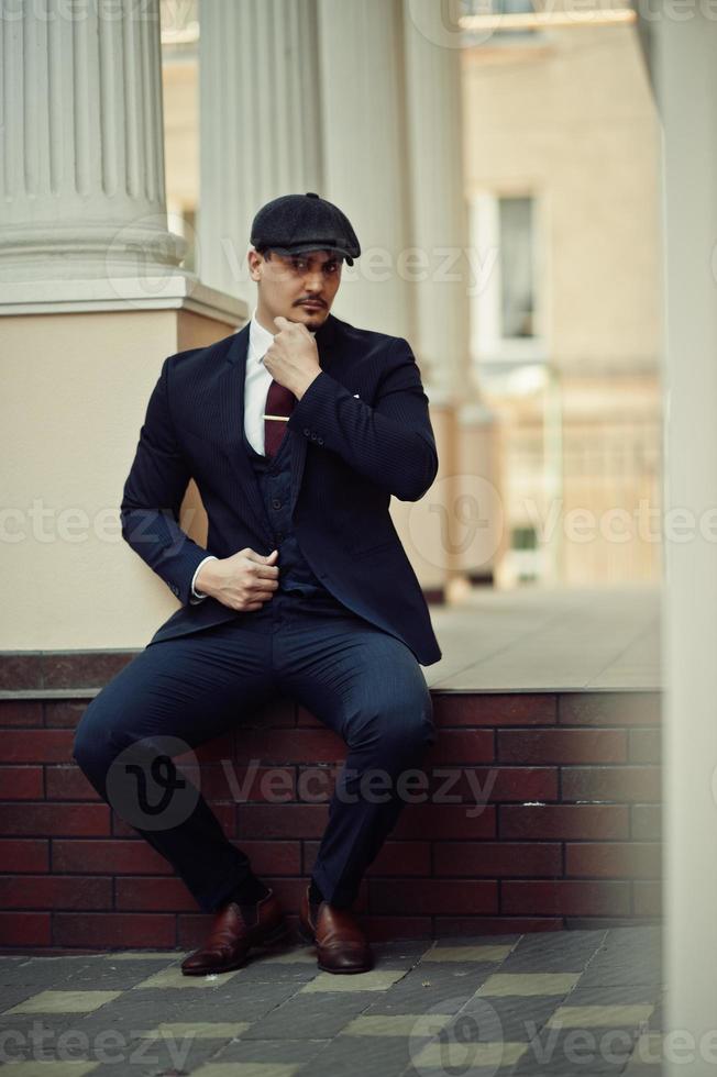 portret van retro Engelse arabische zakenman uit de jaren 1920 met een donker pak, stropdas en platte pet. foto