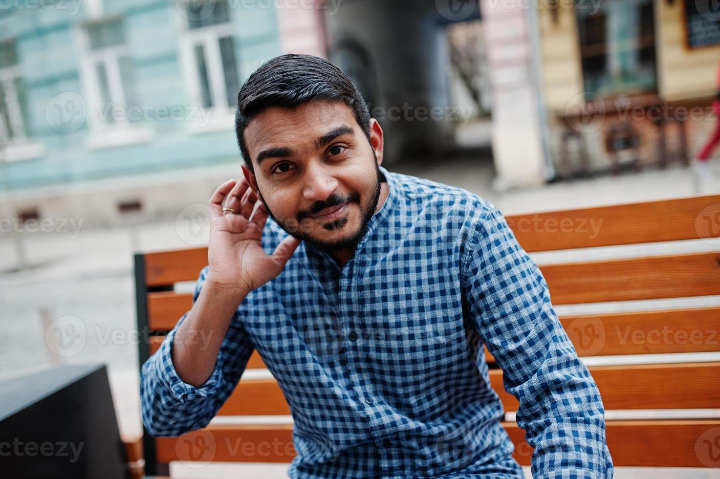 stijlvolle indiase baardmodel man in casual kleding poseerde buiten, zittend op een bankje in de straat van india en denkend over iets te dromen. foto