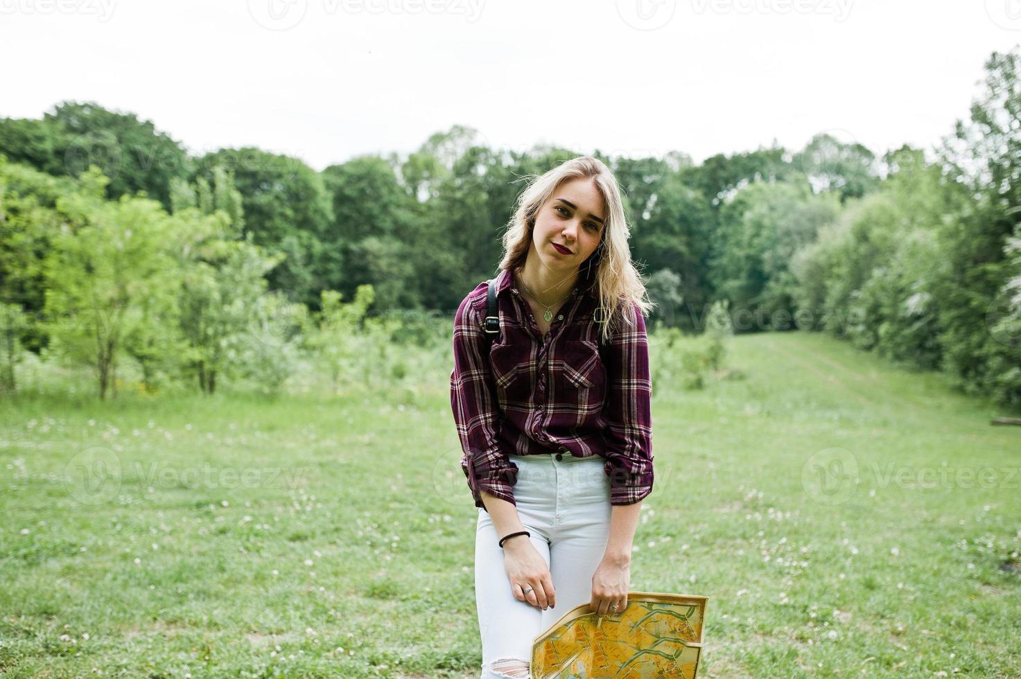 portret van een jonge mooie blonde vrouw in tartan shirt met een kaart in het bos. foto