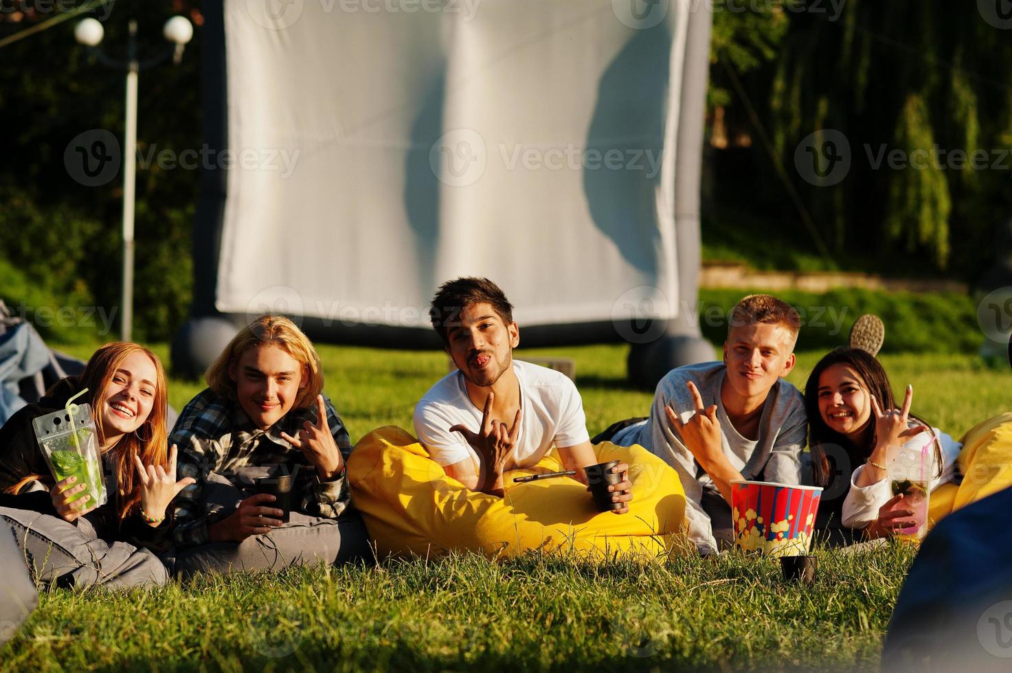 jonge multi-etnische groep mensen kijken naar film op poef in openluchtbioscoop. foto