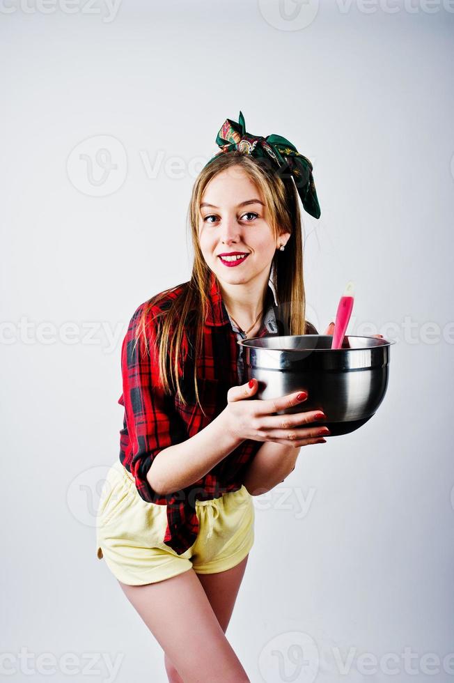 jonge grappige huisvrouw in geruit overhemd en gele korte broek pin-up stijl met pan en keukenlepel geïsoleerd op een witte achtergrond. foto