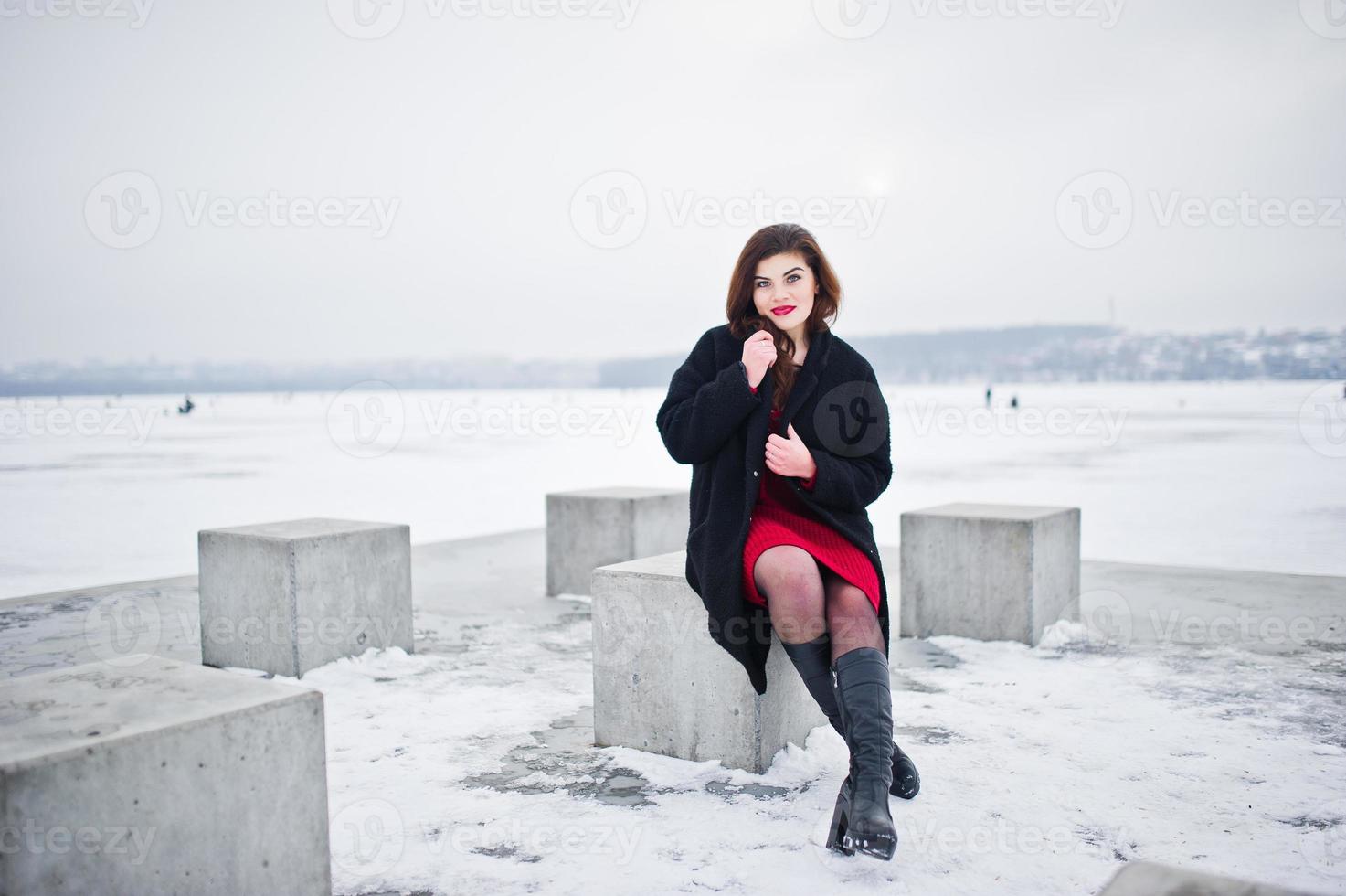 brunette plus size model op rood tegen bevroren meer op winterdag. foto