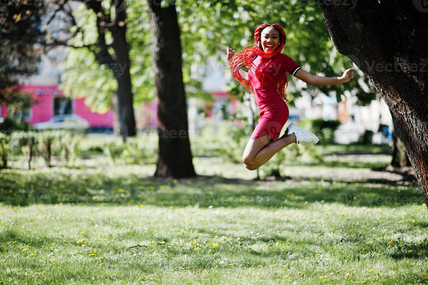 schattig en slank Afrikaans Amerikaans meisje in rode jurk met dreadlocks springen buiten in het voorjaarspark. stijlvol zwart model. foto